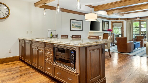 A spacious kitchen with wooden cabinets, a large island with a built-in microwave, pendant lights, and a large window.
