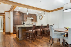 Une cuisine avec des meubles de rangement en bois, un grand îlot central, des tabourets de bar et une table à manger avec des chaises.