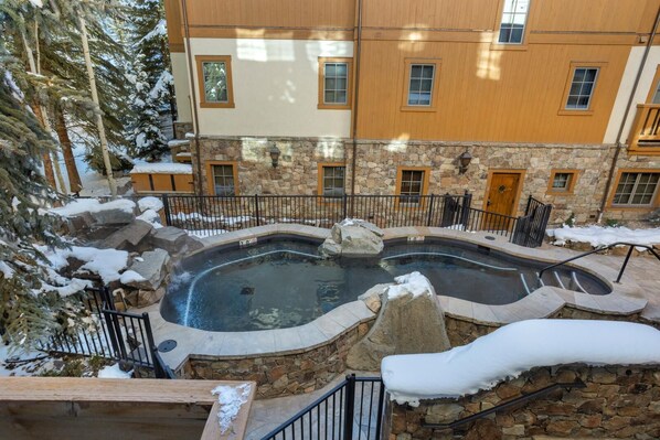 A stone pool with a wooden deck, surrounded by snow-covered trees and a stone wall.