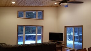 Una sala de estar con televisión, dos ventanas y un ventilador de techo.