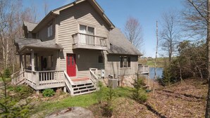 A two-story house with a red door, a balcony, and a porch.