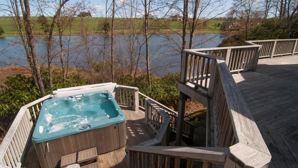 A wooden deck with a hot tub overlooking a lake.