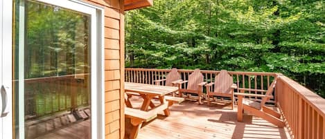 A wooden deck with picnic tables and chairs, surrounded by lush greenery.