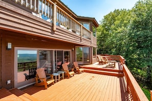 Une maison en bois à deux étages, dotée d’une terrasse, de coins salon extérieurs et de grandes fenêtres.