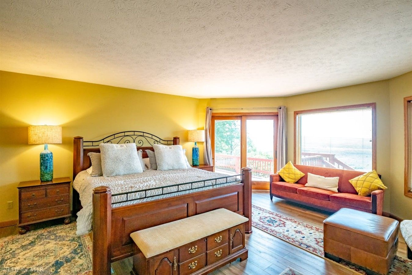 Ein Schlafzimmer mit einem hölzernen Bett, einem Nachttisch, einer Kommode, einem Sofa und einem Fenster mit Blick.