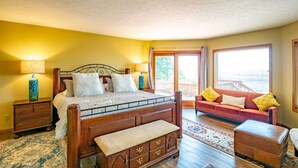 Un dormitorio con cama de madera, mesita de noche, cómoda, sofá y ventana con vistas.