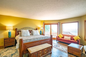 Un dormitorio con cama de madera, mesita de noche, cómoda, sofá y ventana con vistas.