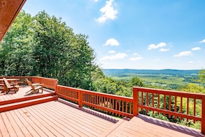 Una terraza de madera con mobiliario exterior y vistas a un paisaje verde.