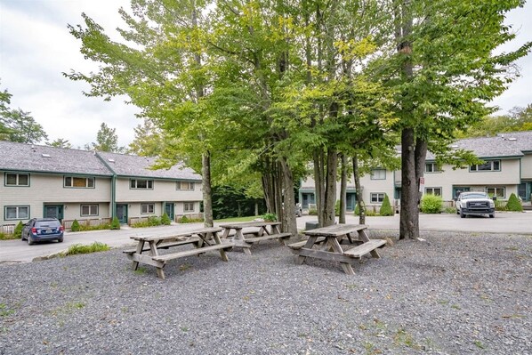 A row of picnic tables in a gravel area with a building in the background.
