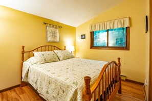 Quarto com cama de madeira, janela com vista, luminária na parede e cortina.
