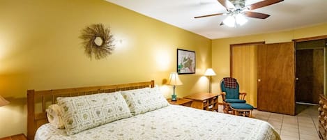 Una habitación de hotel con una cama, un escritorio, una silla, un ventilador de techo y una puerta.
