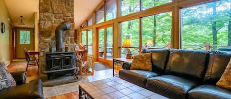 Una sala de estar acogedora con chimenea de piedra, sofá de cuero y amplios ventanales con vistas al exterior.