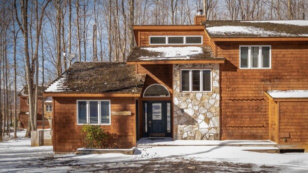 Ein zweistöckiges Holzhaus mit Steinverkleidung, einer Haustür und einer kleinen Veranda.