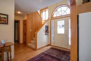 Un escalier en bois menant à un deuxième étage, une porte avec une pancarte indiquant «Remontée mécanique», et un tapis sur le sol.