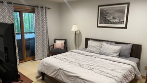 Ein Schlafzimmer mit einem Bett, einem Sessel, einem Fernseher und einem gerahmten Bild an der Wand.