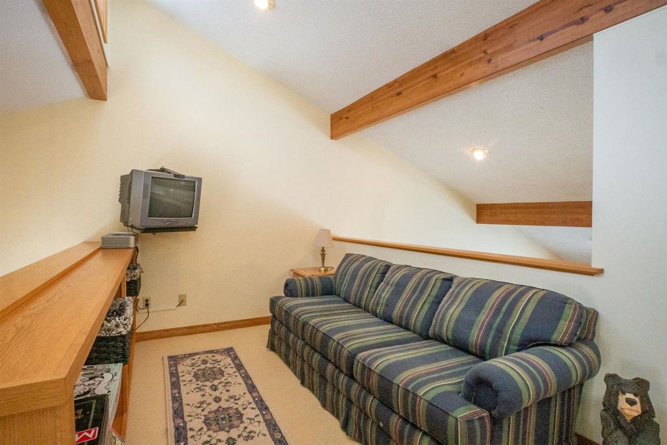 A cozy room with a wooden bench, a striped sofa, a television, and a small table with a lamp.