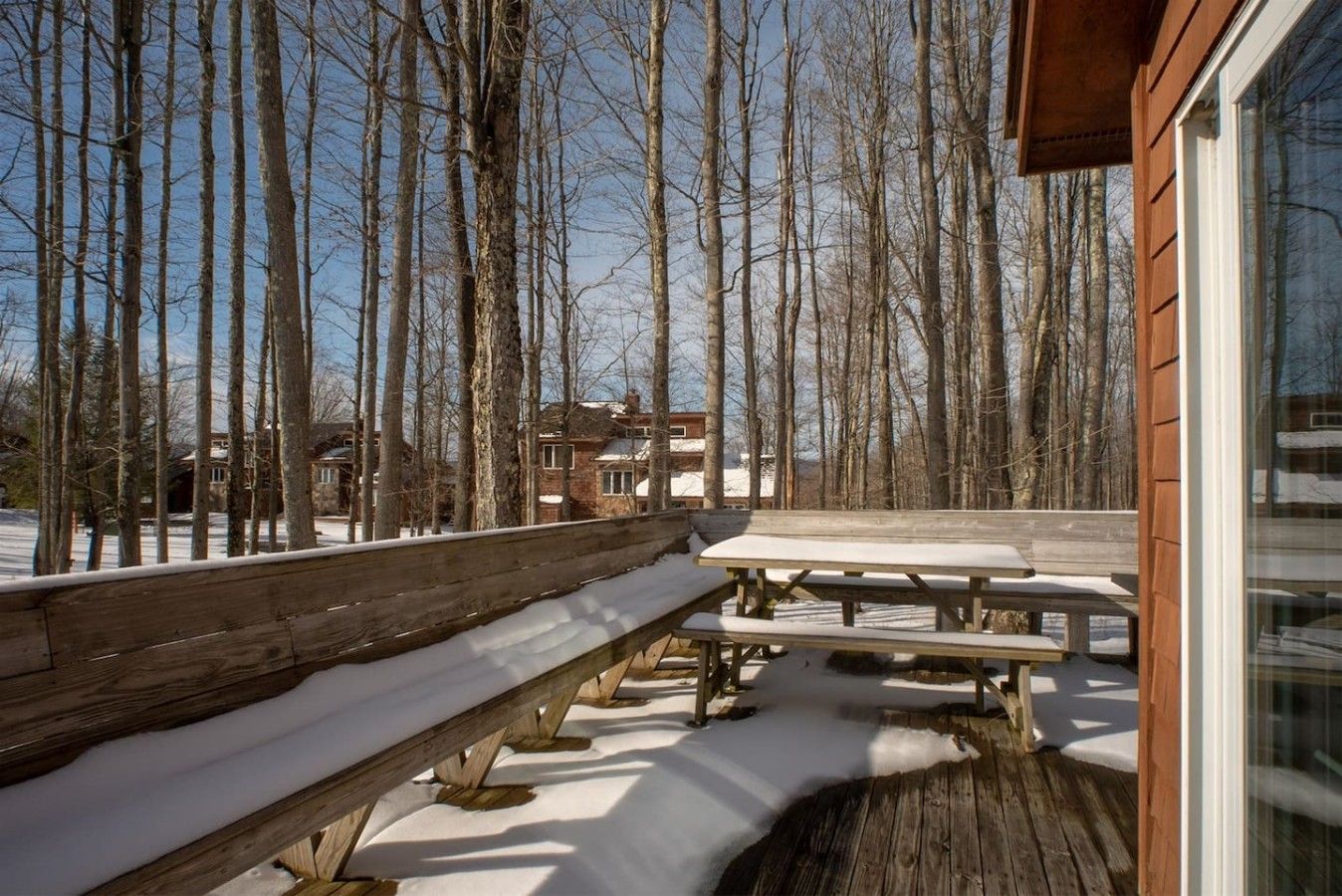 Eine Holzterrasse mit Bänken und Picknicktischen, umgeben von verschneitem Boden und kahl stehenden Bäumen.