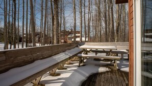 Eine Holzterrasse mit Bänken und Picknicktischen, umgeben von verschneitem Boden und kahl stehenden Bäumen.