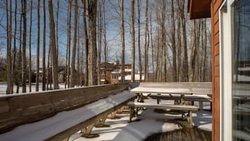 A wooden deck with benches and picnic tables, surrounded by snow-covered ground and leafless trees.