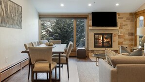 Una sala de estar moderna con chimenea, un comedor con un ventanal grande y un ventilador de techo.
