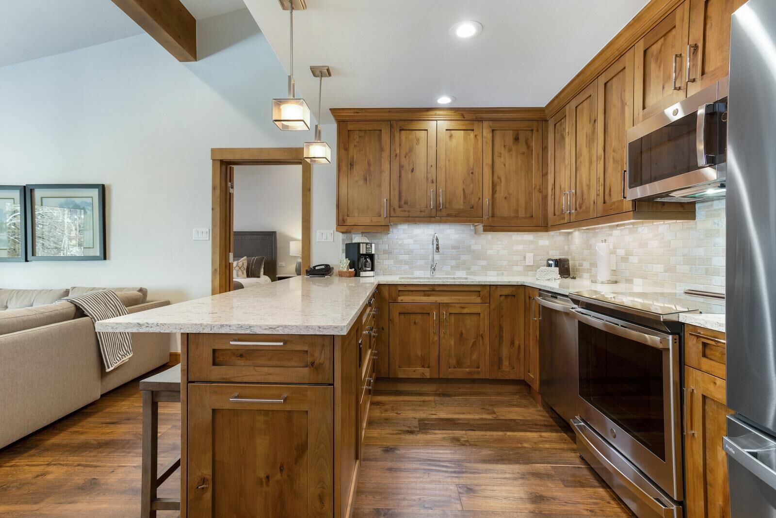 A modern kitchen with wooden cabinets, a large island, stainless steel appliances, and a view of the living area.