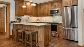 Una cocina moderna con armarios de madera, electrodomésticos de acero inoxidable y una isla central con taburetes de bar.