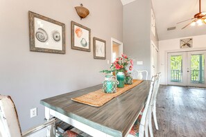 Ein Essbereich mit einem langen Holztisch, gerahmten Bildern an der Wand und Blick ins Freie durch eine Tür.