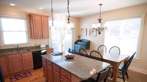 A kitchen with granite countertops, wooden cabinets, a dining table with chairs, and pendant lighting.