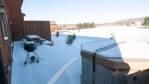 A backyard with a wooden deck, a barbecue grill, and a hot tub.