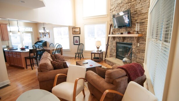 A spacious living room with a fireplace, a kitchen in the background, and a dining area.