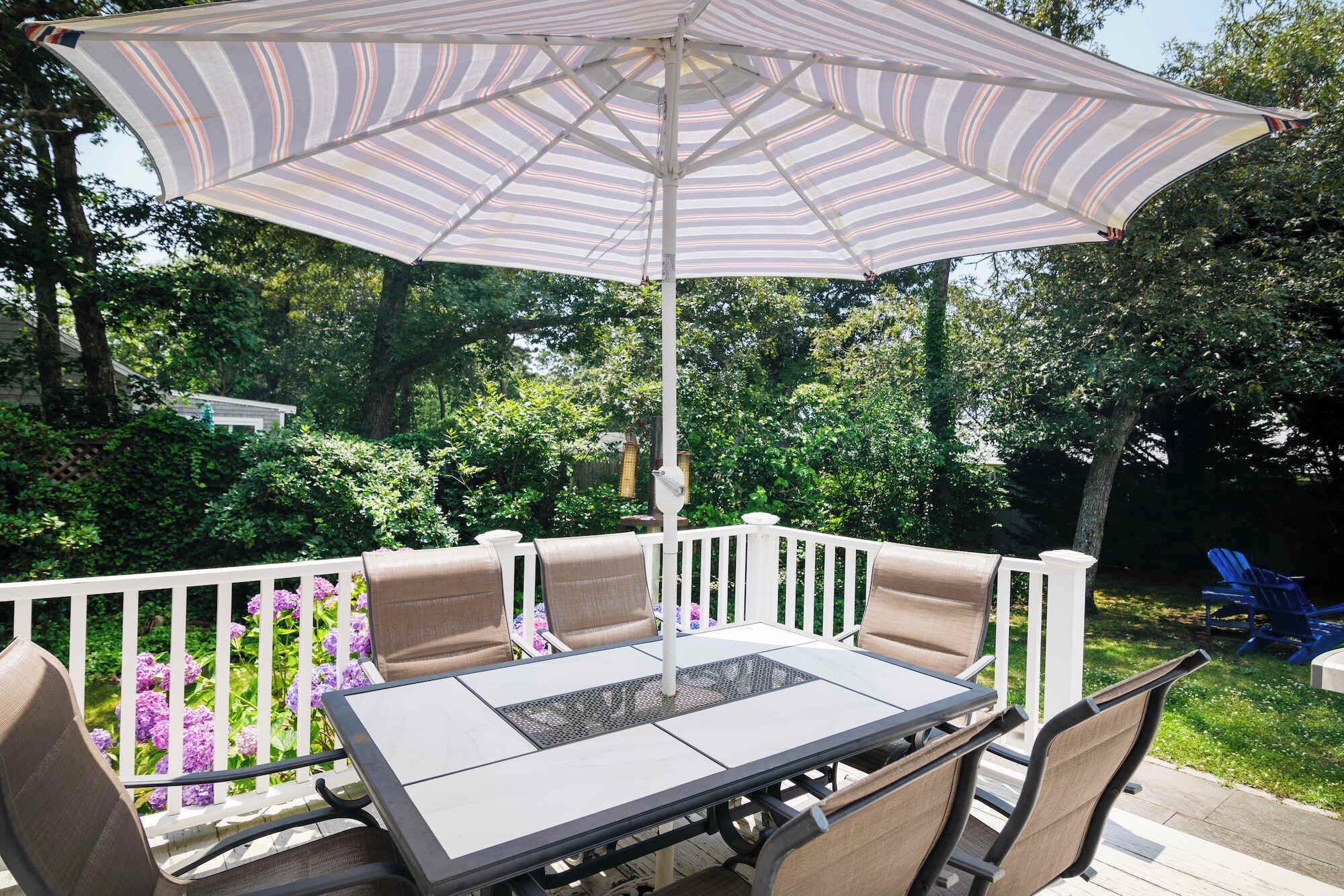 An outdoor patio with a table and chairs, a striped umbrella, and a white railing.