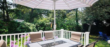 An outdoor patio with a table and chairs, a striped umbrella, and a white railing.