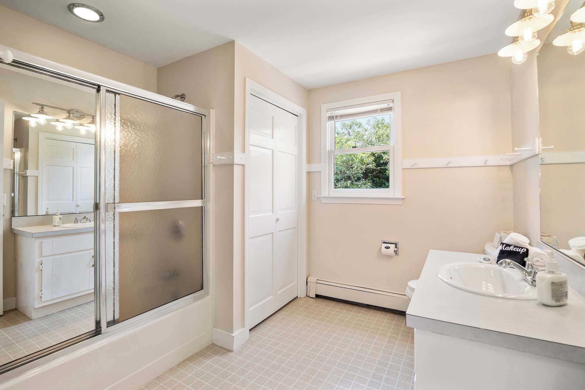 A bathroom with a glass shower enclosure, a white sink, and a window providing natural light.