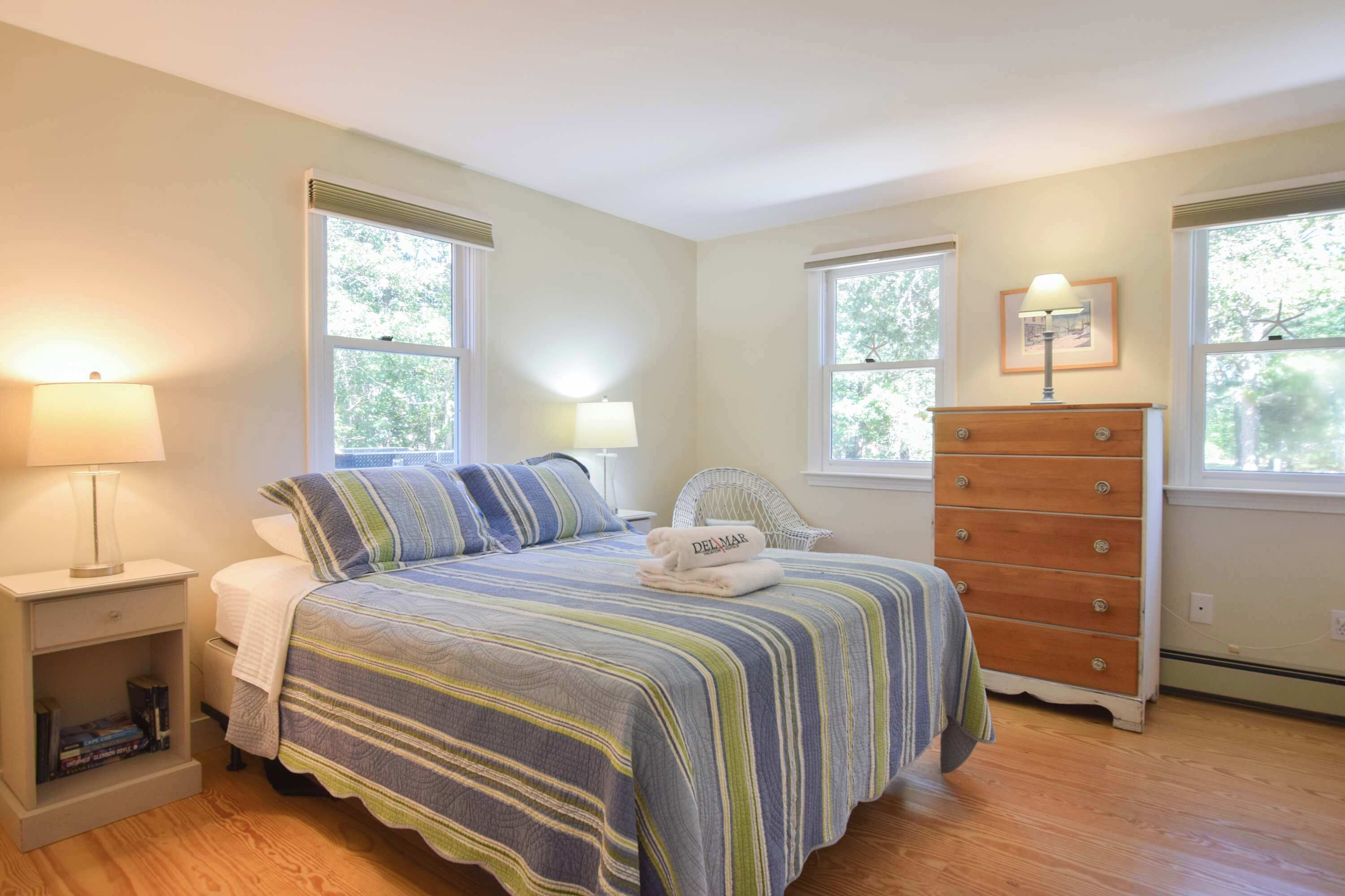 A bedroom with a bed, nightstands, a dresser, and windows.
