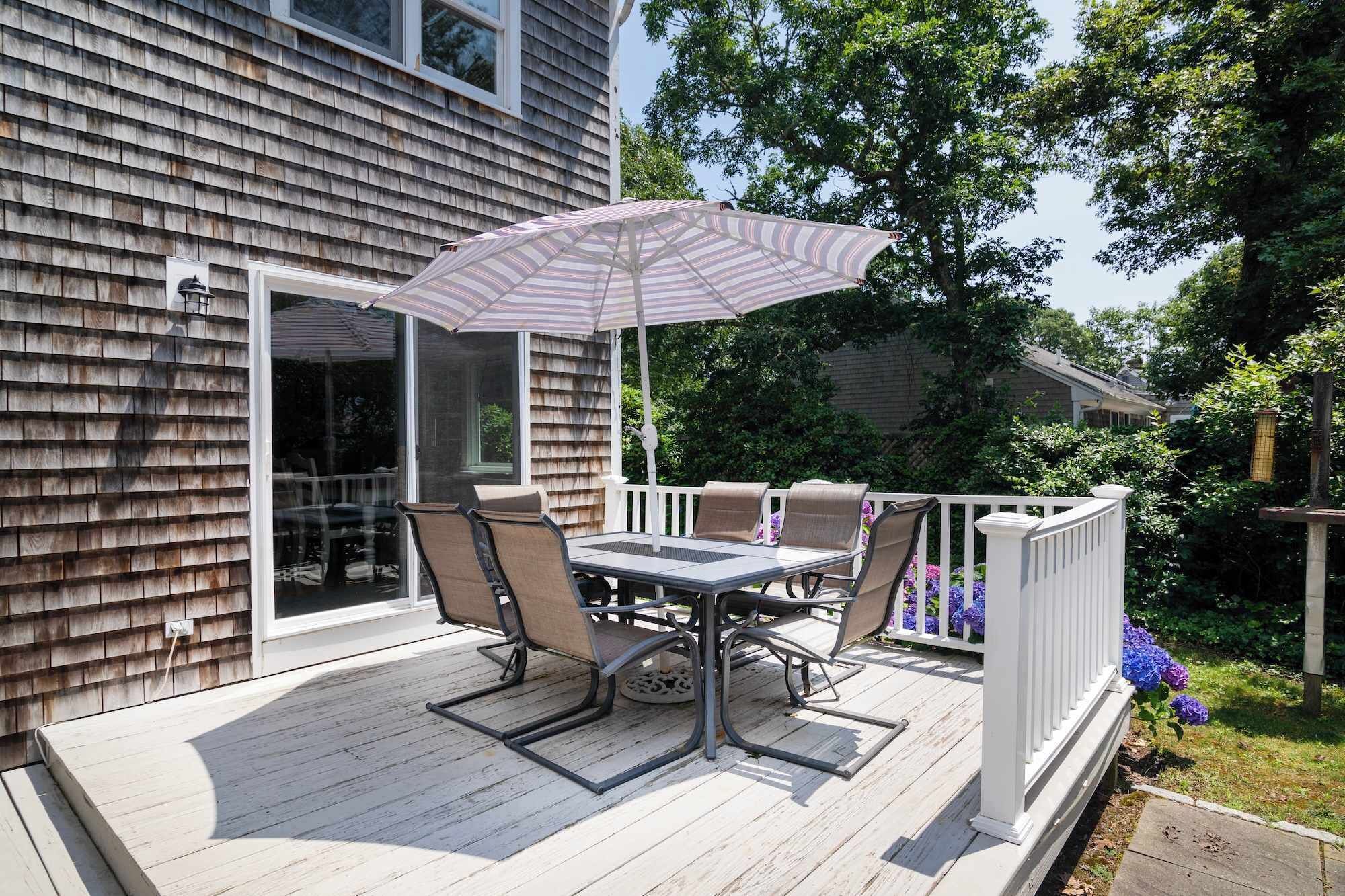 Une terrasse couverte avec une table et des chaises, un parasol à rayures et une balustrade blanche.