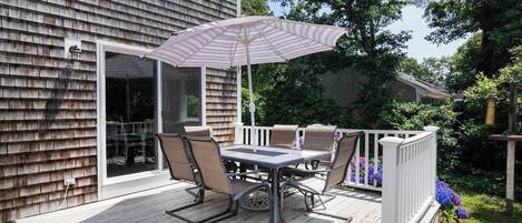Une terrasse couverte avec une table et des chaises, un parasol à rayures et une balustrade blanche.
