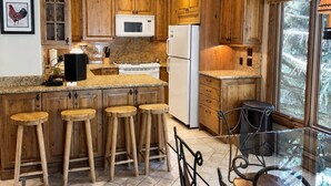 A kitchen with wooden cabinets, a microwave, a refrigerator, and a glass dining table with chairs. - Riva Ridge 720 | 2BR Vail Village (Vail)