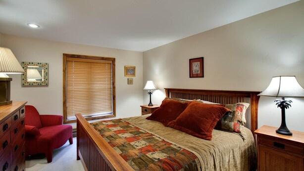 A bedroom with a bed, a dresser, a chair, and a window with blinds. - Riva Ridge 720 | 2BR Vail Village (Vail)