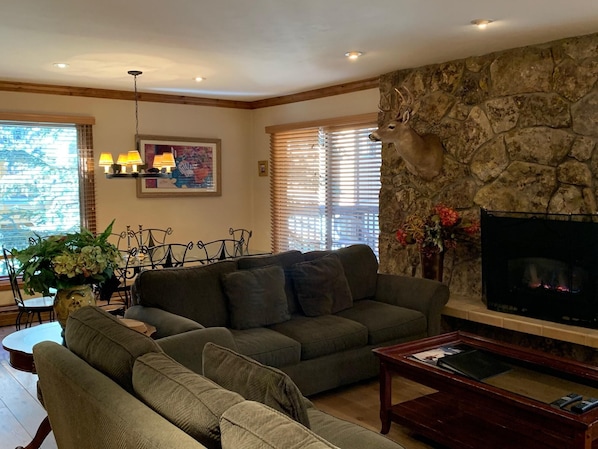 A living room with a stone fireplace, a sofa, a coffee table, and a dining area with a table and chairs. - Riva Ridge 720 | 2BR Vail Village (Vail)