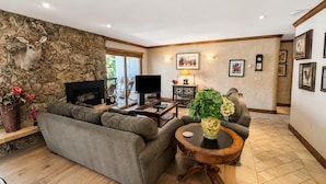 A living room with a stone wall, a fireplace, a sofa, a television, and a coffee table. - Riva Ridge 720 | 2BR Vail Village (Vail)