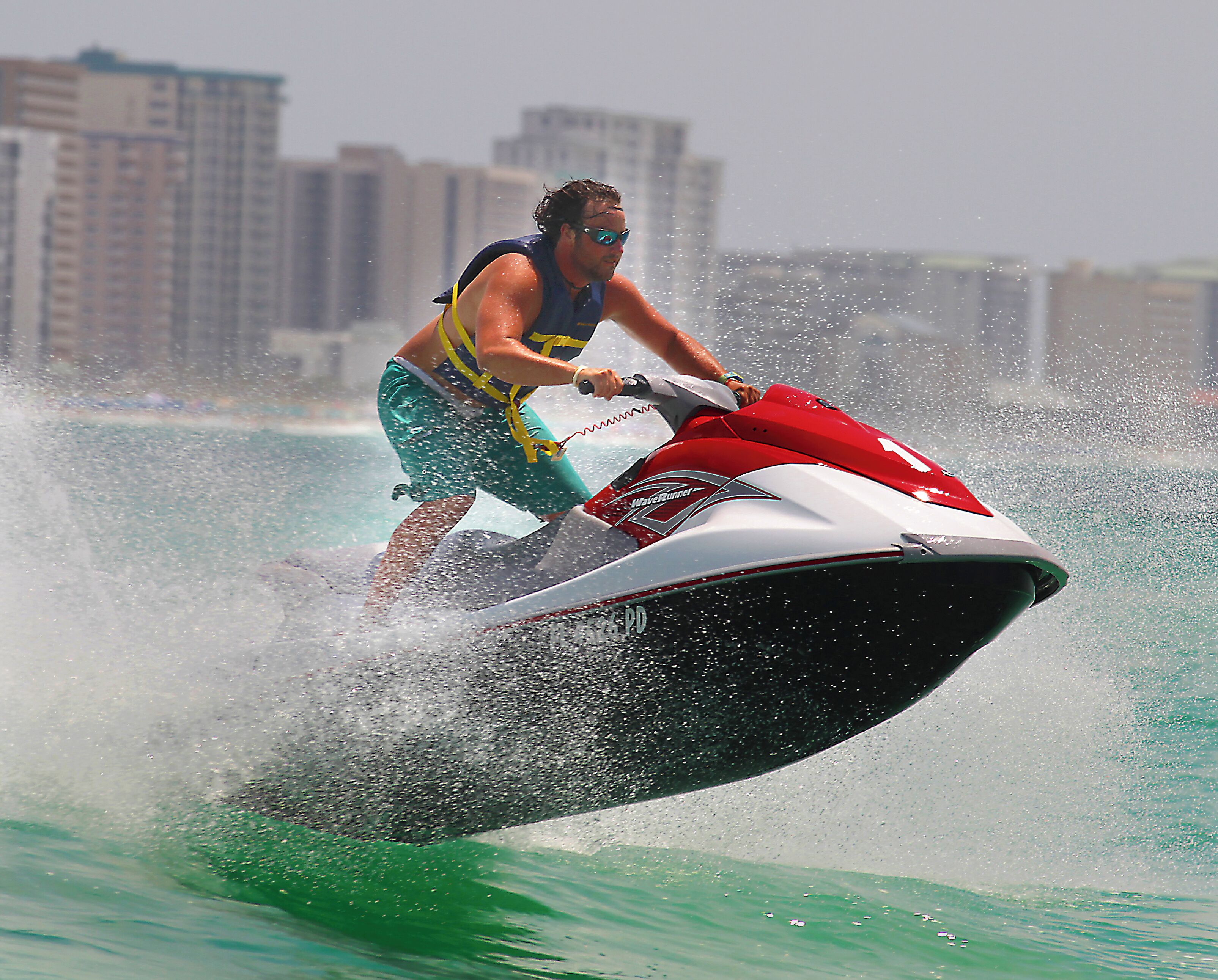A person jet skiing on a body of water with buildings in the background.