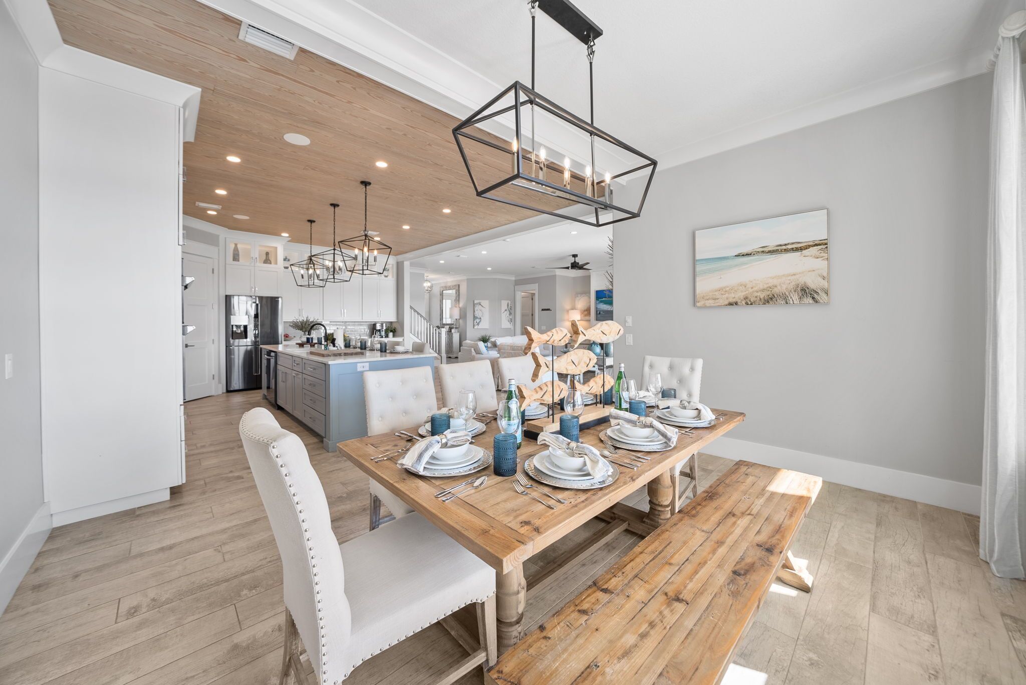 A dining area with a wooden table set for four, a chandelier, and a beach-themed painting on the wall.