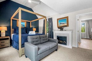 Un dormitorio con cama con dosel, chimenea, sofá gris y un cuadro de un barco en la pared.