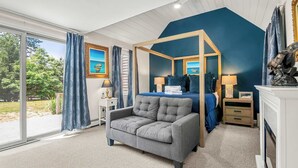 Une chambre à coucher avec un lit à baldaquin, un fauteuil gris, une table de chevet avec une lampe et un tableau accroché au mur.