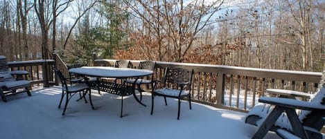 Un muelle cubierto de nieve con una mesa y sillas, rodeado de árboles.