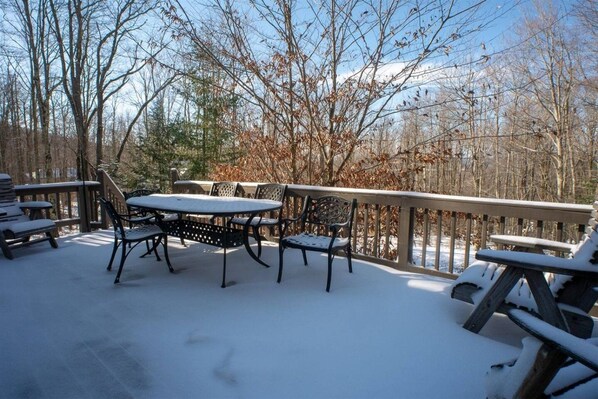 A snow-covered deck with a table and chairs, surrounded by trees.