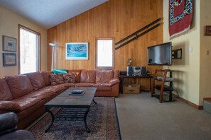 A living room with a leather sofa, a coffee table, a TV, and a wooden wall.
