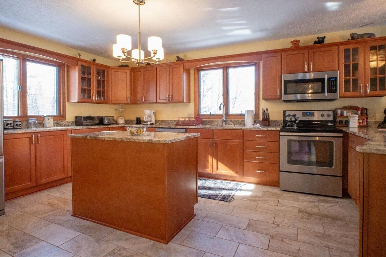 A kitchen with wooden cabinets, a central island, a microwave, and an oven.