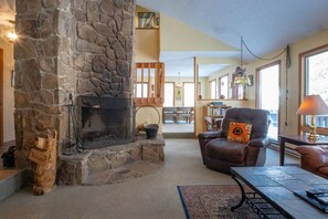 Una chimenea de piedra con un adorno de cabeza de oso, un sillón de cuero con un cojín estampado, y una mesa con un control remoto.