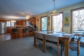 A spacious kitchen with a dining area, large windows, and a ceiling fan.